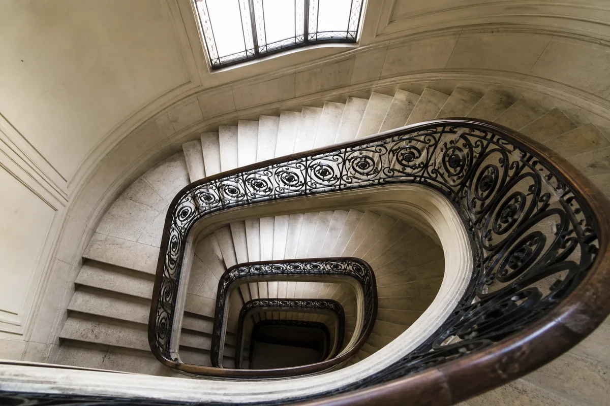 Cage d’escalier ancienne en pierre claire avec rampe en fer forgé noir