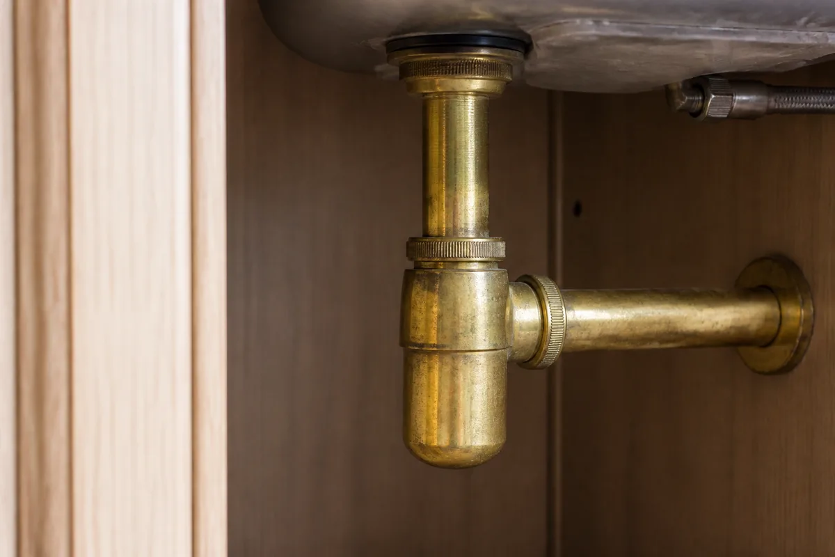 Siphon en laiton fixé sous un évier dans un placard de cuisine